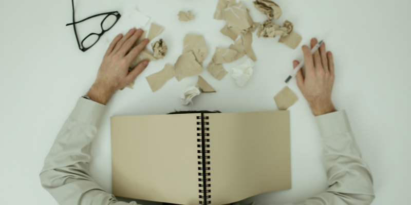 Man in business attire face down on a desk with a notebook covering his head Man in business attire face down on a desk with a notebook covering his head