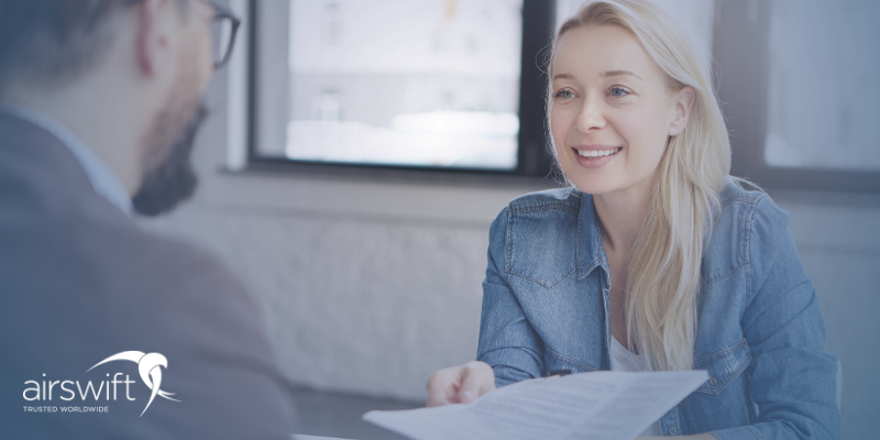 A blonde woman hands over resume document to a man during a job interview