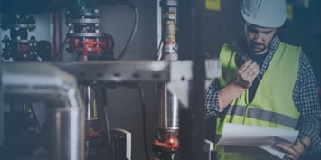 Chemical engineering professional reviewing process documents and operating a handheld radio beside industrial piping and equipment, representing chemical engineering career paths and chemical engineering salary opportunities in the energy and manufacturing sectors.