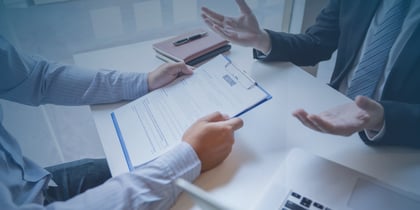 Two business professionals seated at a table, reviewing documents on a clipboard, discussing staff augmentation strategies.