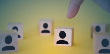 A person indicates a collective of individuals depicted on wooden blocks, illustrating the focus on compliance in cross-border contractor management.