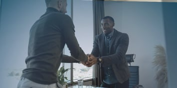 Two professionals shaking hands in an office setting, representing collaboration in international technical staffing efforts.