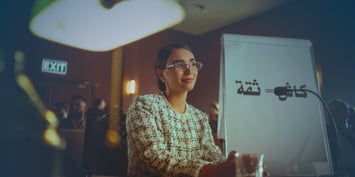 A woman in glasses is at a table with a laptop