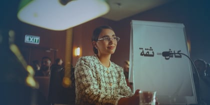 A woman in glasses is at a table with a laptop
