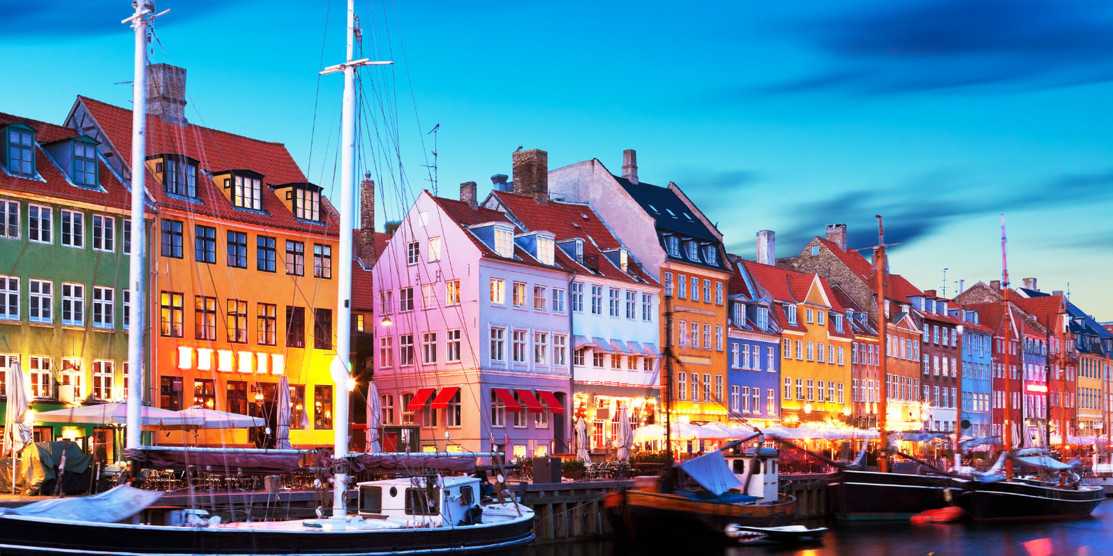 Wide angle shot of a row of colourful buildings in Denmark behind a marina with boats
