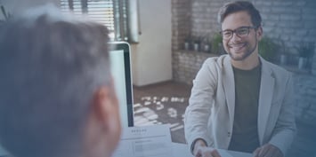A smiling man wearing formal attire shakes hands with a potential employer in an office setting