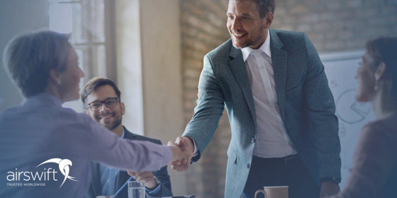 An employee shaking hands with his employer, both smiling in a comfortable setting