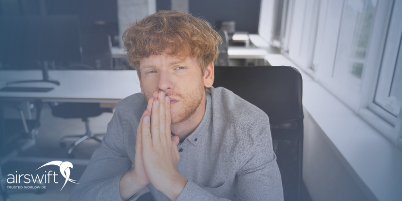 A young man wearing a suit sits in an office, looking nervous ahead of his first job interview with a new company