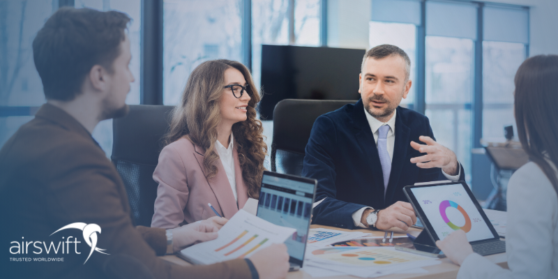 Colleagues smile in a meeting whilst discussing report metrics, visible on printouts and a laptop screen