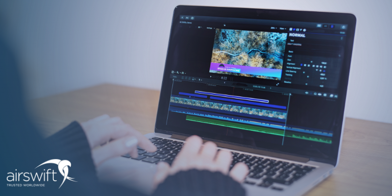 A laptop is open on video editing screen. We can see a woman's hands with silver nail polish typing on the keys.