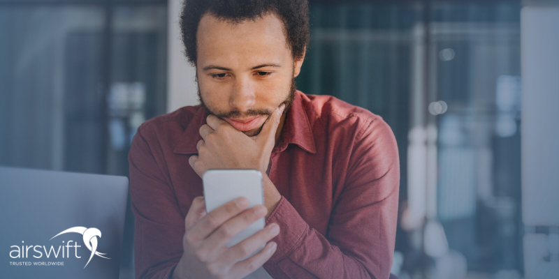 A man wearing a red shirt scrolls on his mobile phone in an office setting
