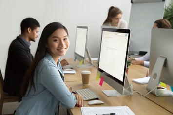 Young woman sitting at her computer and smiling at the camera in an office setting