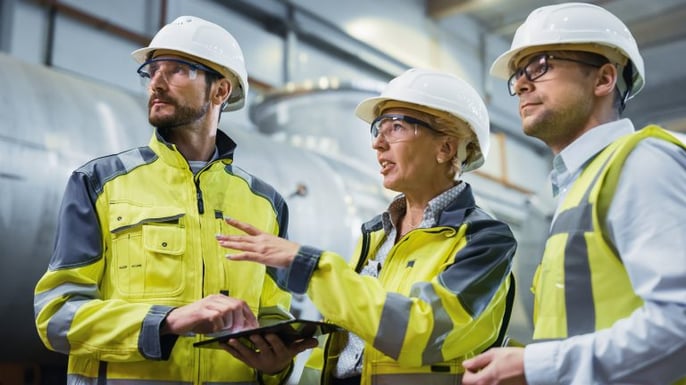 three engineers in hi-vis and hardhats having a conversation inside a facility with a tablet