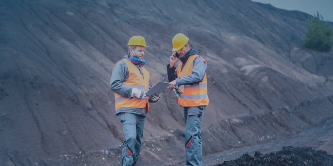 Two men in hi-vis and hardhats at mine reading off clipboard and on the phone