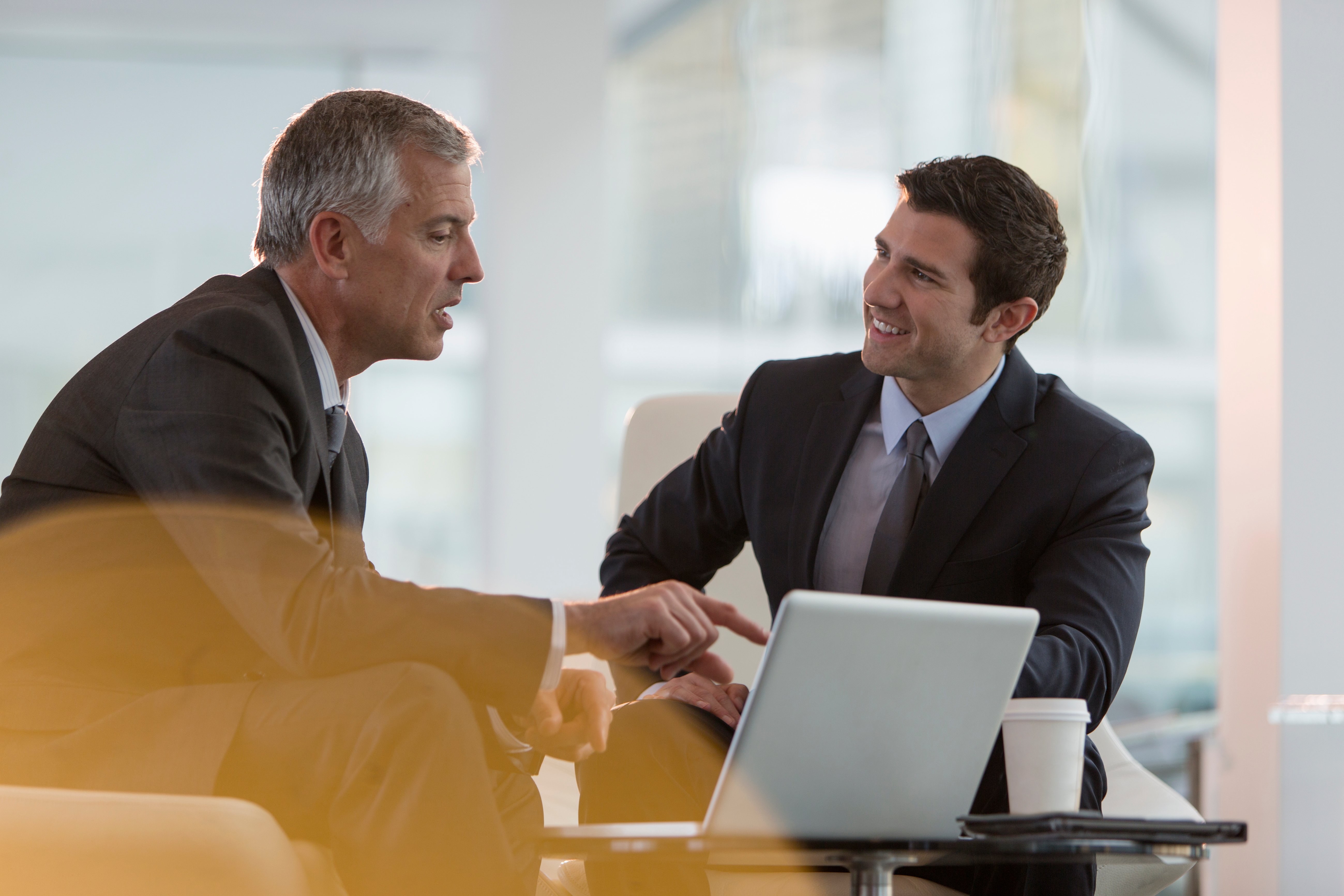Two well-dressed men in suits sat down in front of a laptop having a meeting