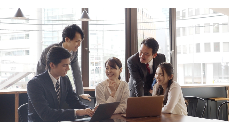 People in business attire in an office around two laptops having a discussion