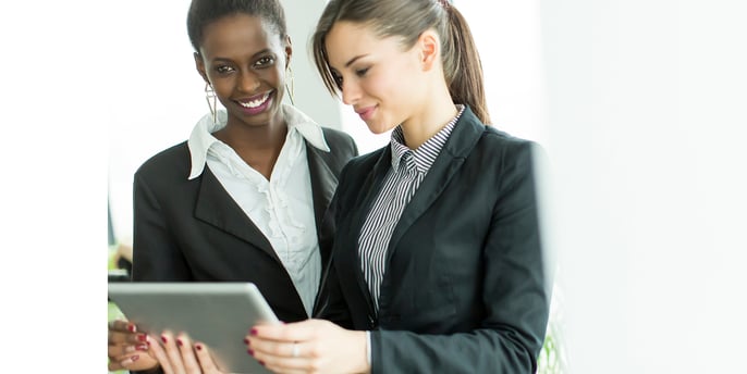 Women dressed in business attire holding a tablet and having a discussion