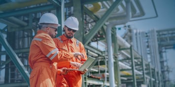 Two energy workers review project plans at an industrial facility, highlighting workforce management challenges in energy projects.