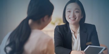 Two women converse, one in a business suit, representing a professional exchange in a corporate setting.