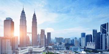 Skyline of Kuala Lumpur with the Petronas Twin Towers at the foreground against a backdrop of clear blue skies.