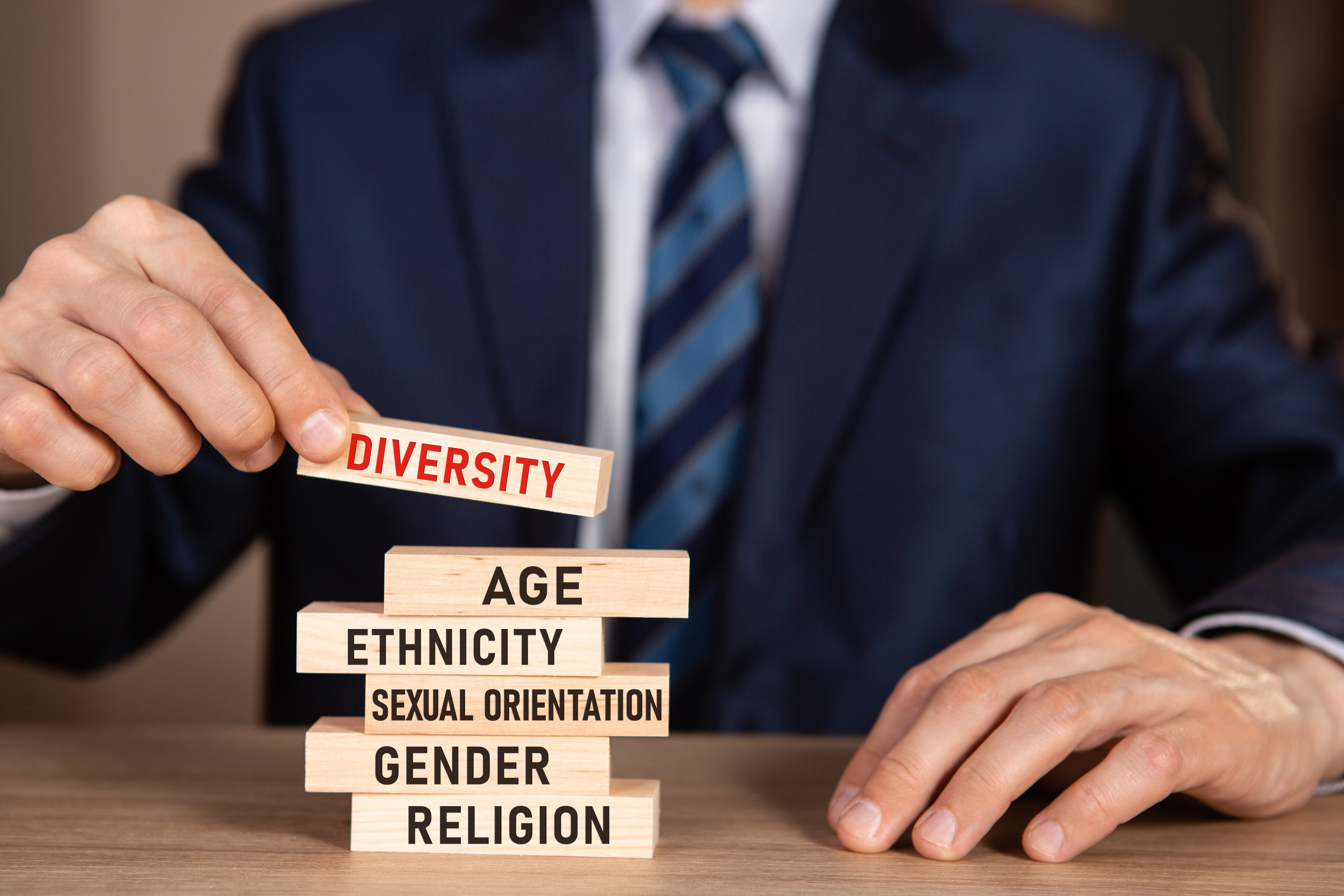 Diversity concept. Business man building stack from wooden blocks with text Diversity, Age, Ethnicity, Sexual Orientation, Gender, Religion.