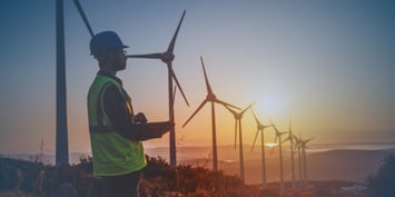 Wind farm technician inspecting turbines at sunset in a renewable energy facility.