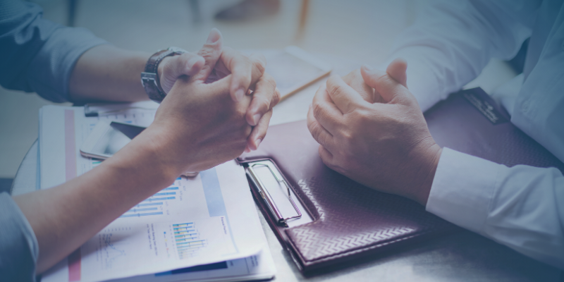 Two professionals clasping their hands over a table filled with documents, indicating a collaboration or agreement in workforce strategy.