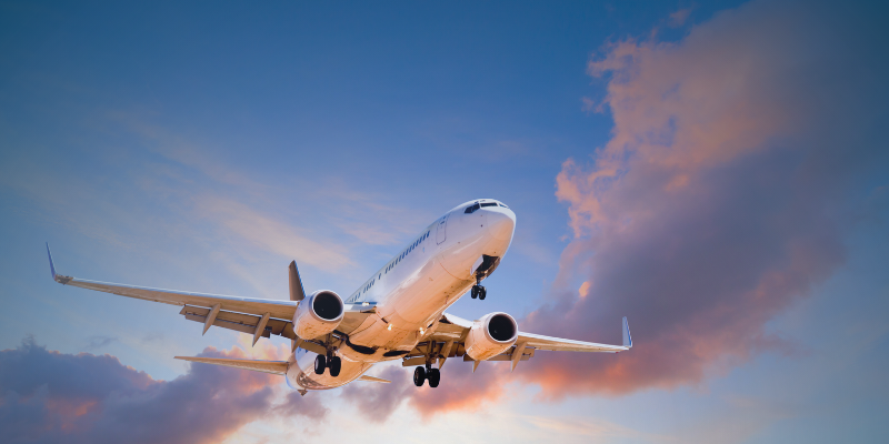 An aircraft in flight against a vibrant sky filled with clouds, illustrating the concept of travel and job opportunities.