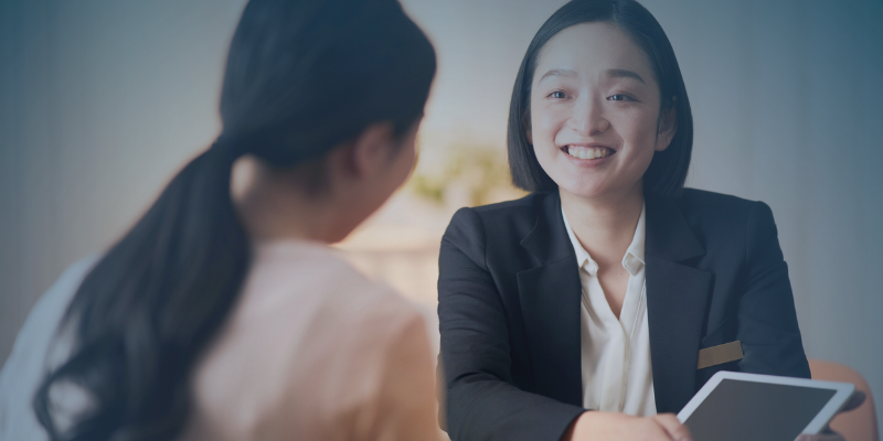 Two women converse, one in a business suit, representing a professional exchange in a corporate setting.