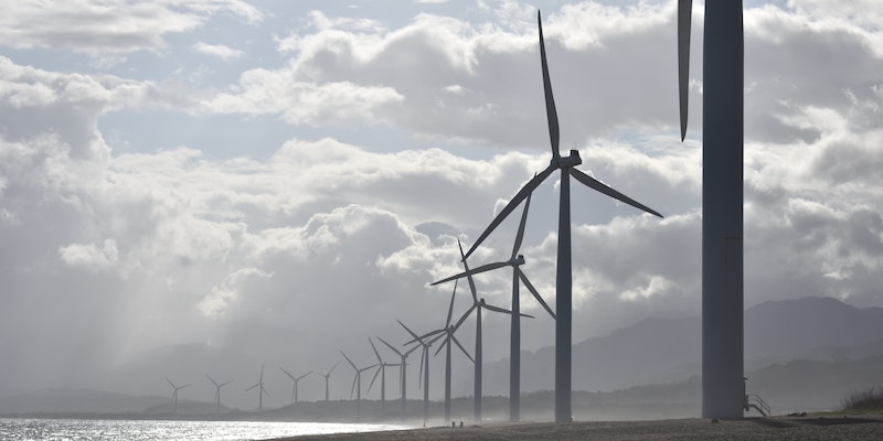 Row of wind turbines along a coastline against cloudy skies