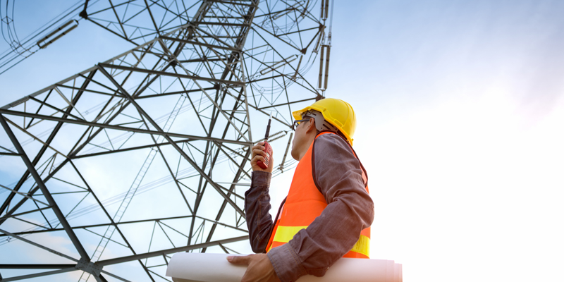  Engineer with hardhat and plans under electricity pylon representing power employment trends